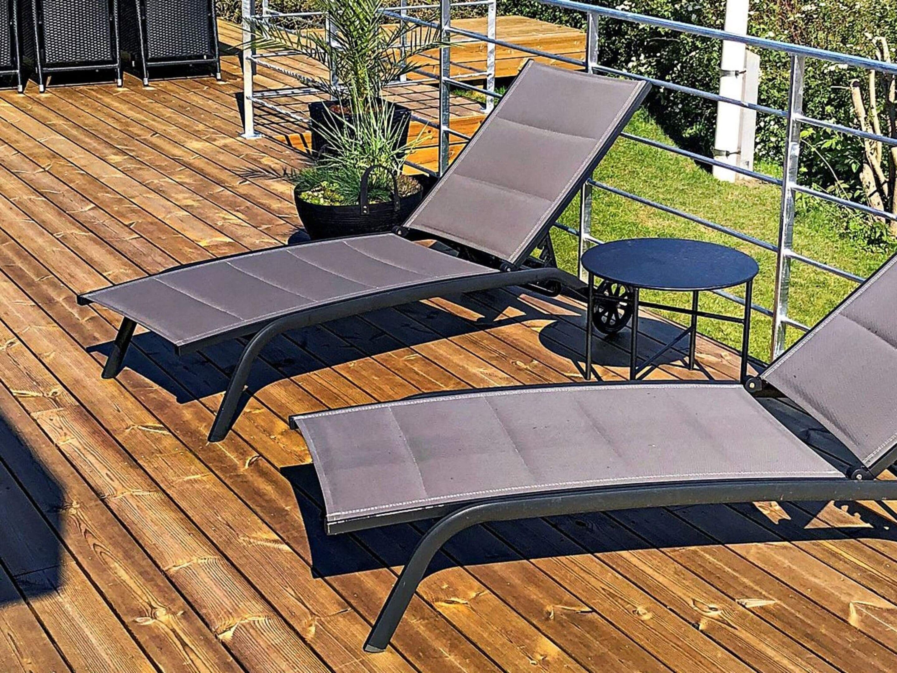 A wooden deck with two lounge chairs and a small round table.