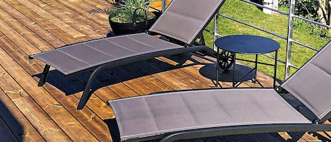 Eine Holzterrasse mit zwei Liegestühlen und einem kleinen runden Tisch.