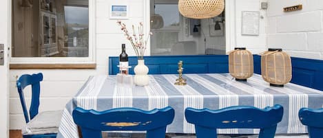 A dining area with a table set for four, blue chairs, a striped tablecloth, a hanging light fixture, and wall decorations including framed pictures and a fish-shaped ornament.