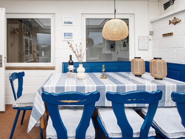A dining area with a table set for four, blue chairs, a striped tablecloth, a hanging light fixture, and wall decorations including framed pictures and a fish-shaped ornament.