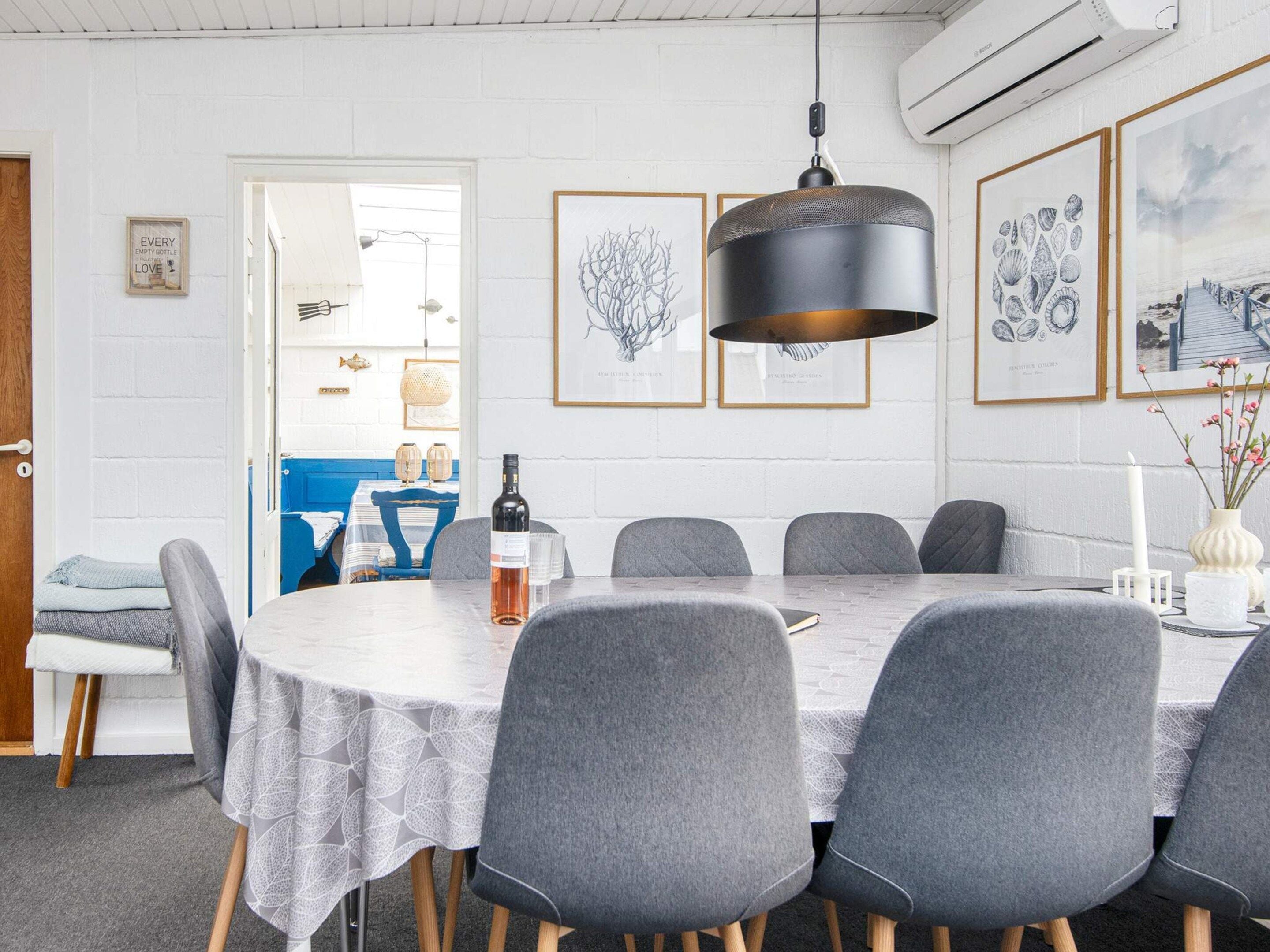 Un coin repas avec une table ronde, des chaises grises, un luminaire suspendu et des œuvres d’art encadrées accrochées au mur.
