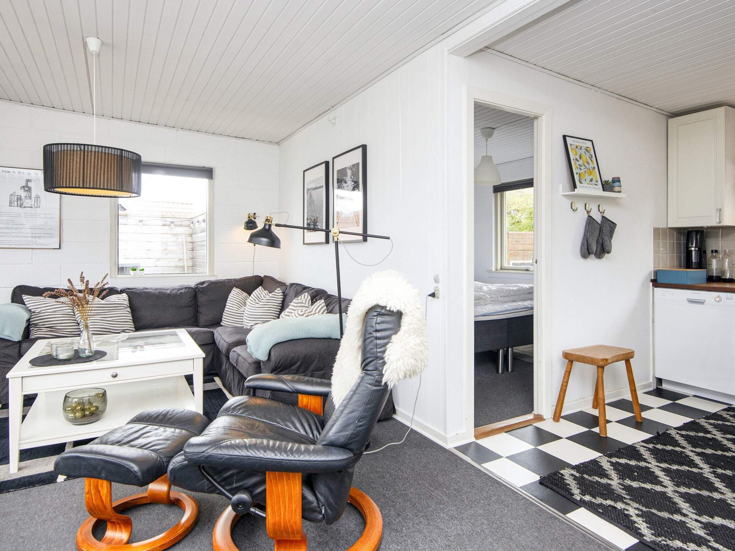En moderne stue med en sofa, en læderstol i sort farve, et sofabord og et spiseområde med et køkken i baggrunden.