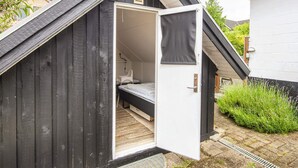 A small, dark wooden structure with a white door open, revealing a bed and a chair inside. - 4 Star Holiday Home in Hejls (Hejls)