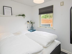 A bedroom with a bed, a bedside table with a lamp, a window with a view, and a framed quote on the wall.