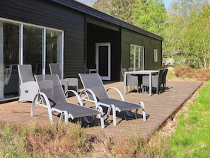 A modern outdoor deck with lounge chairs and a table, surrounded by a wooden deck and vegetation.