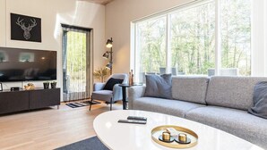 A modern living room with a large TV, grey sofa, and a coffee table with decorative items. - 5 Star Holiday Home in Hadsund (Hadsund)
