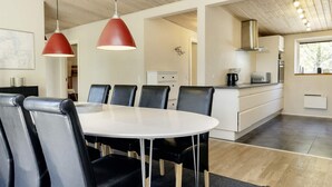A modern kitchen with a central island, black chairs around a white table, and red pendant lights. - 5 Star Holiday Home in Hadsund (Hadsund)