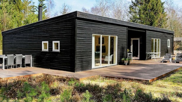 A modern black building with large sliding glass doors, a deck, and outdoor seating. - 5 Star Holiday Home in Hadsund (Hadsund)