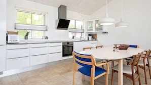 A modern kitchen with white cabinets, a built-in oven, a microwave, and a dining area with a round table and wooden chairs. - 5 Person Holiday Home in Farso (Farso)