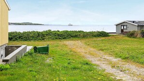 A coastal property with a grassy lawn, a concrete pathway, and a small building with a metal roof. - 5 Person Holiday Home in Farso (Farso)