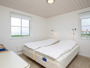 Quarto com uma cama de solteiro, duas janelas, uma mesa e uma luminária no teto.