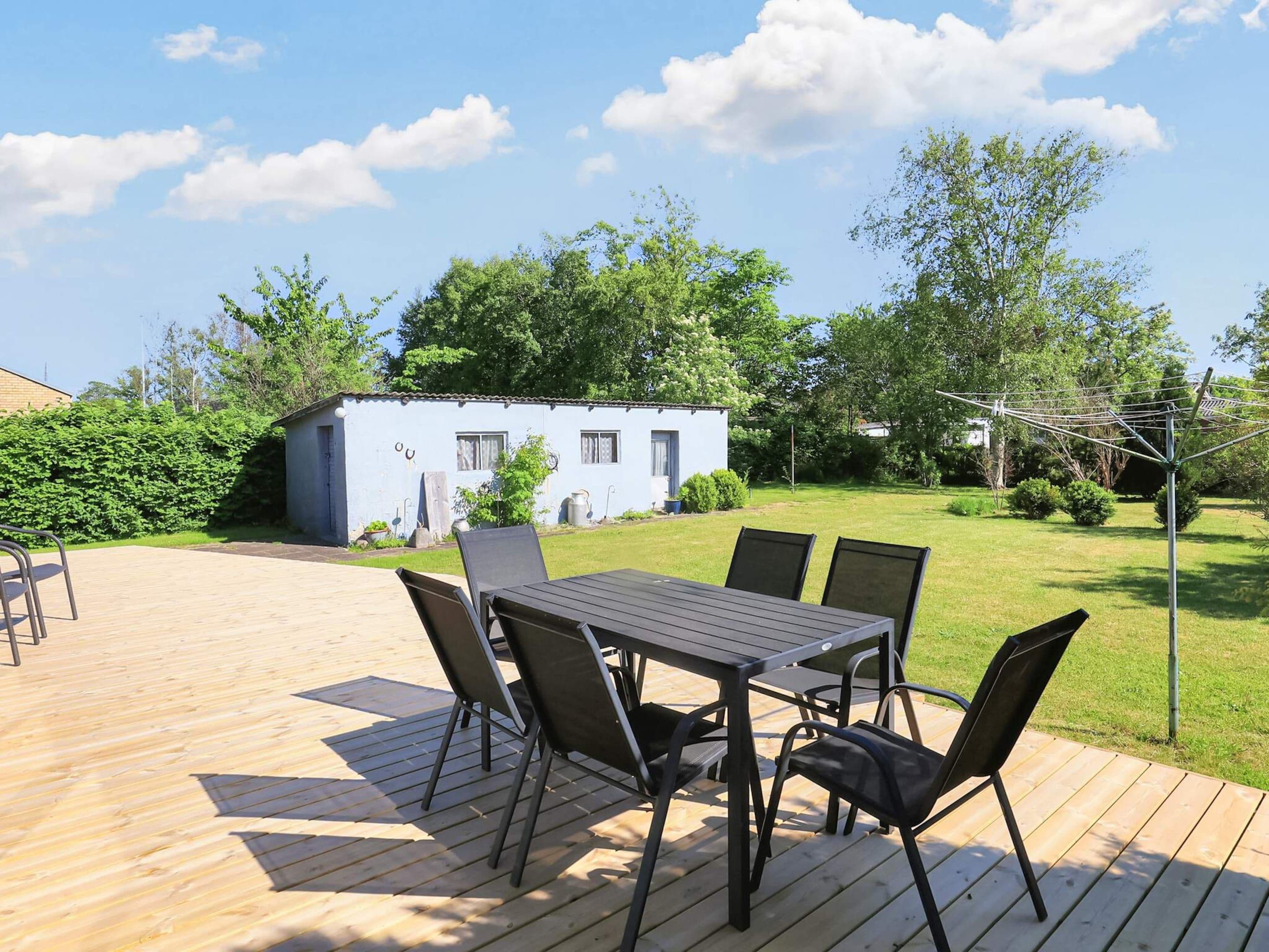 A deck with a table and chairs, a small blue building, and a grassy area with trees.