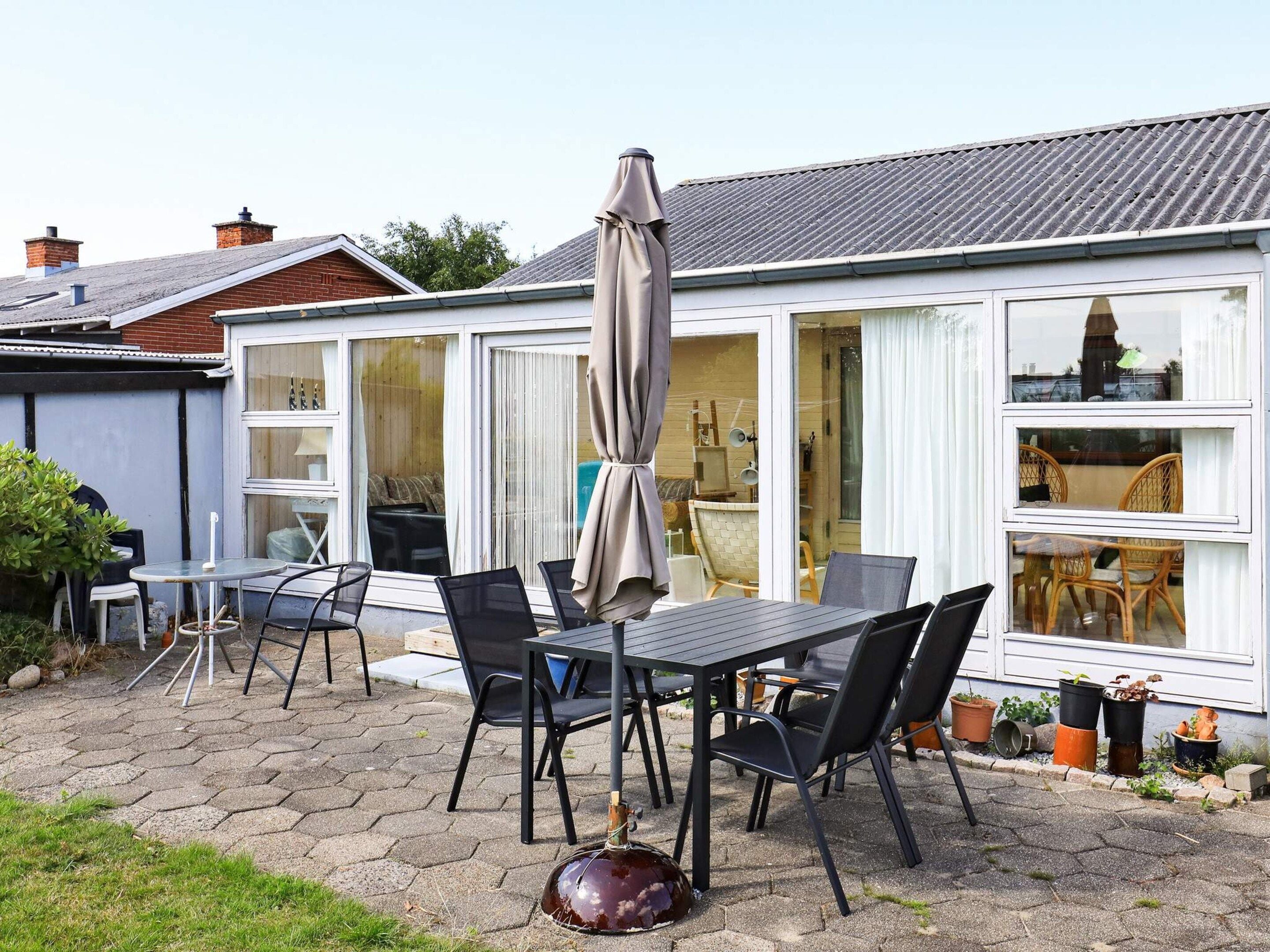 A patio with a table and chairs, a large umbrella, and potted plants.