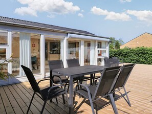 A covered outdoor area with a table and chairs, a glass door entrance, and a brick building in the background.