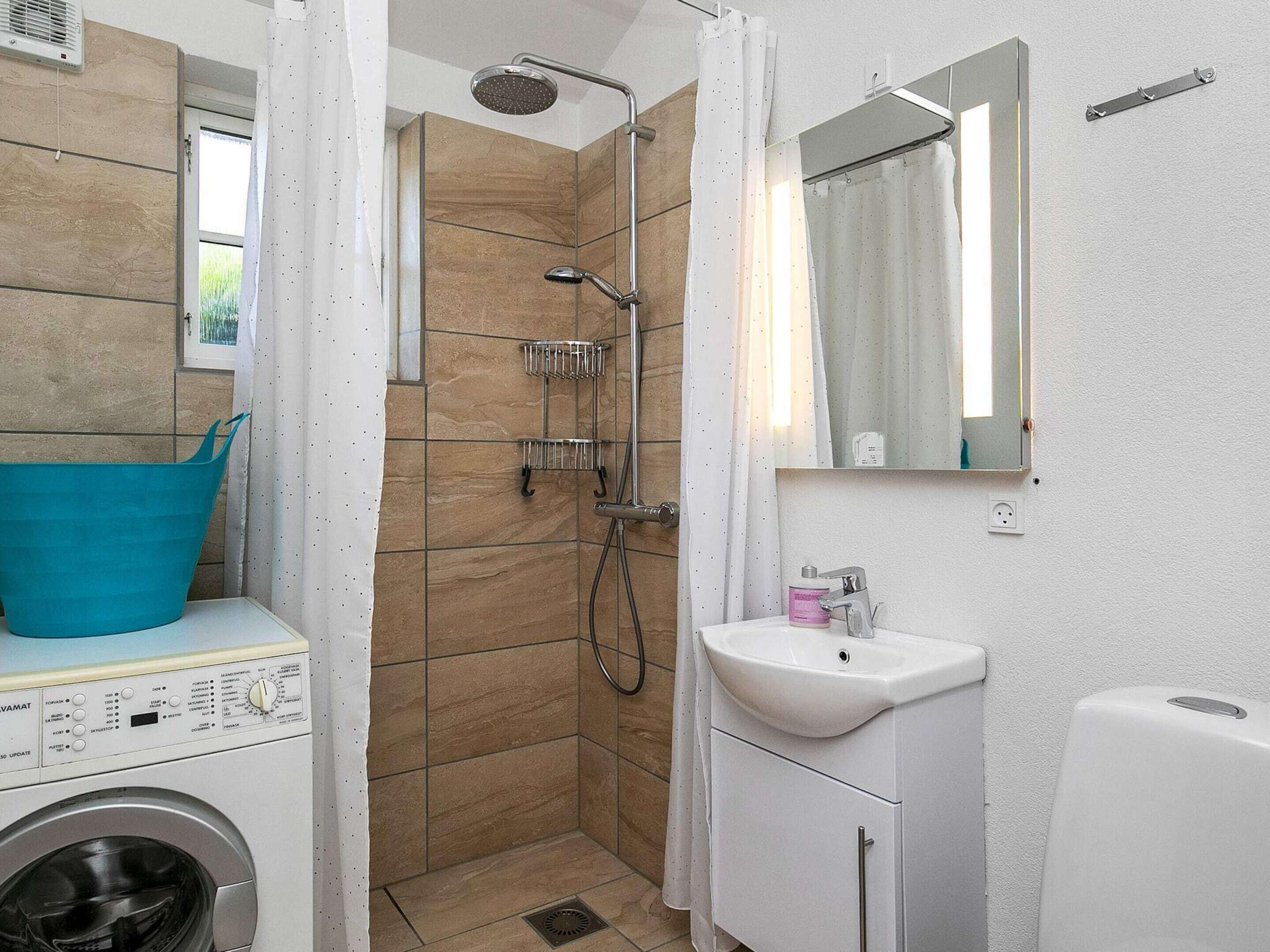 A compact bathroom with a washing machine, a shower with a handheld showerhead, a sink, and a mirror.