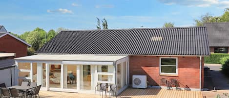 A modern house with a wooden deck, a glass-enclosed patio, and a red brick exterior.