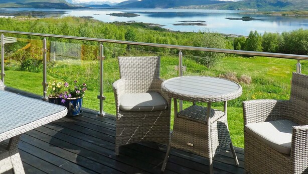 A deck with wicker furniture overlooking a lake and mountains. - 7 Person Holiday Home in Skutvik (Hamaroy)