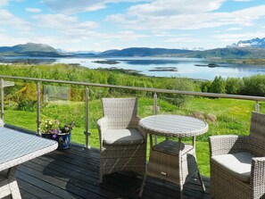 A deck with wicker furniture overlooking a lake and mountains. - 7 Person Holiday Home in Skutvik (Hamaroy)