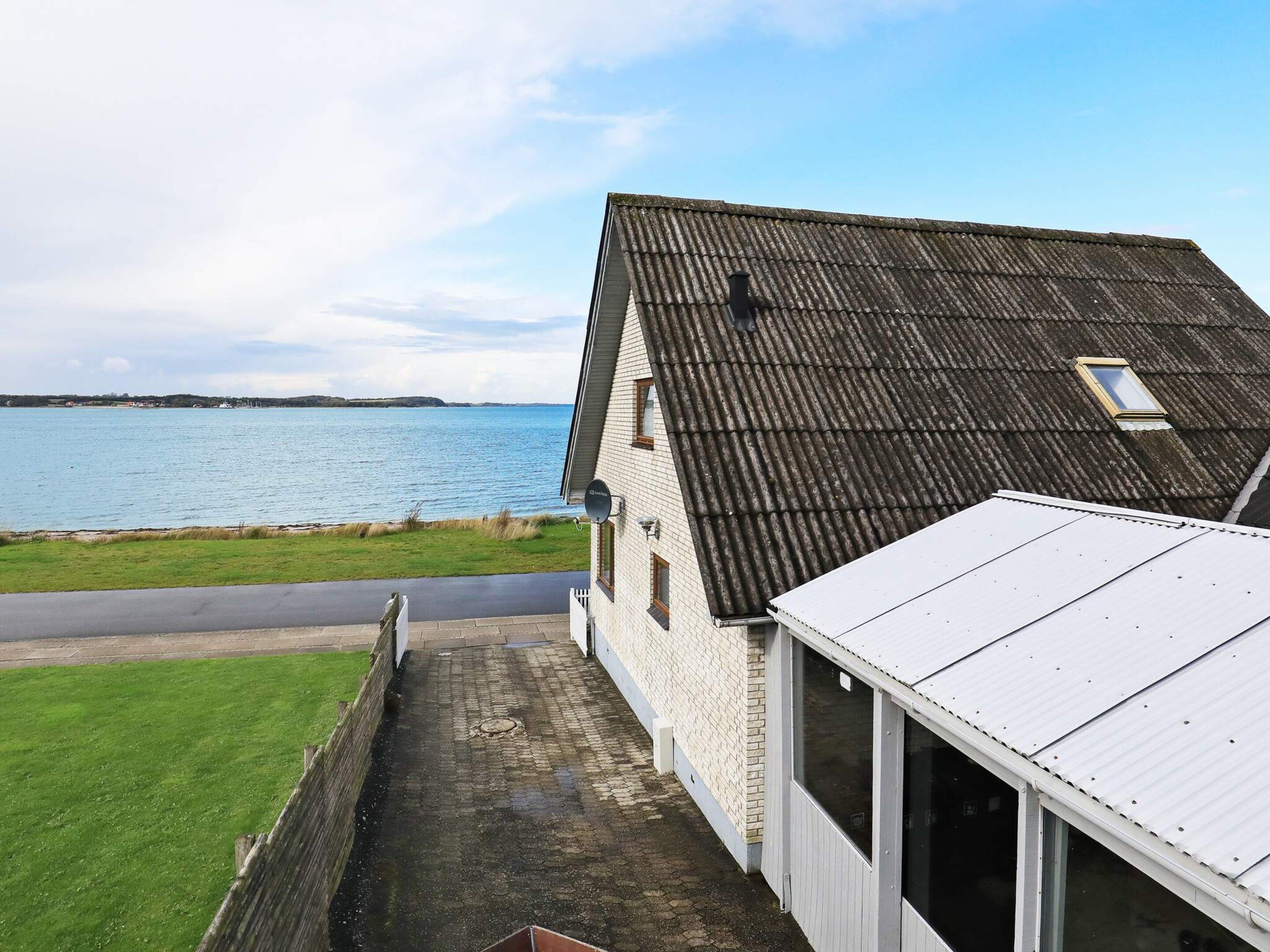 A coastal property with a view of the sea, a paved driveway, and a white building with a grey roof.