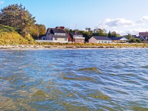 A coastal property with multiple houses along the shoreline, clear water in the foreground, and a grassy area with trees. - 10 Person Holiday Home in Farso (Farso)