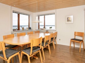 A spacious dining area with a large wooden table and chairs, large windows with a view of the water, and a pendant light. - 10 Person Holiday Home in Farso (Farso)