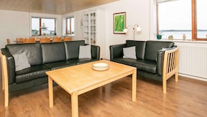Een ruime woonkamer met twee zwarte leren banken, een houten salontafel en uitzicht op zee door grote ramen.