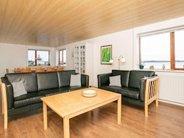 A spacious living room with two black leather sofas, a wooden coffee table, and a view of the sea through large windows.