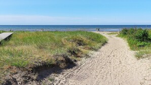 A sandy beach path leading to the sea with grassy areas and a clear sky.