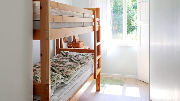 A bunk bed with a floral quilt, a wooden side table, and a window with curtains.