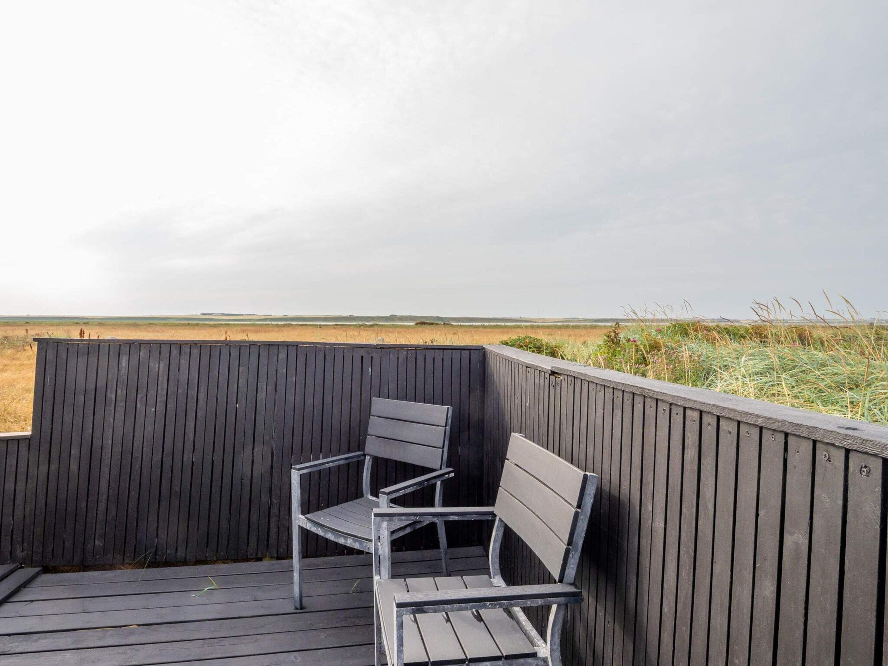 Terraza de madera con dos sillas de metal y vista a un paisaje llano.