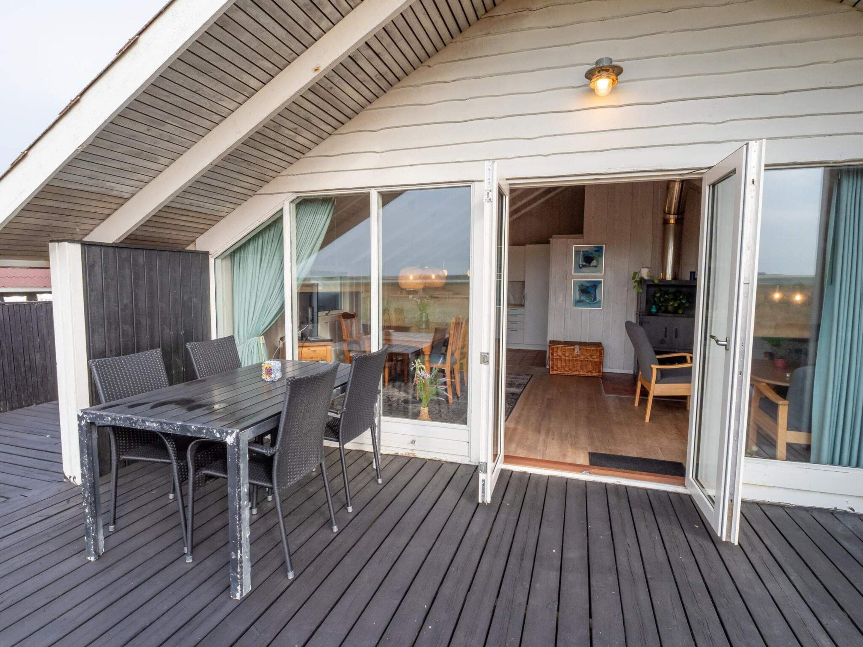 A covered outdoor area with a dining table and chairs, a sliding glass door leading to an interior space, and a ceiling light fixture.