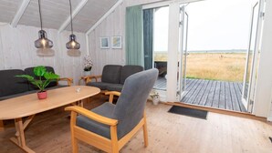 A modern interior with a wooden floor, a round table, grey sofas, and a view of a field through a glass door. - 6 Person Holiday Home in Harboore (Harboore)