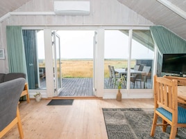 Una habitación con piso de madera, un sofá, una mesa de comedor con sillas, un televisor y vistas al exterior a través de amplias puertas de vidrio.