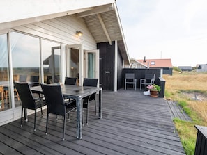 Une terrasse en bois avec une table et des chaises, un pot de fleurs et une vue sur un bâtiment doté d’un toit en pente.