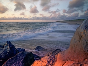 Una playa con olas, rocas y una costa lejana.