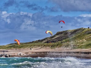 A coastal area with waves crashing onto rocks, a grassy hill, and several people engaged in outdoor activities. - 6 Person Holiday Home in Harboore (Harboore)