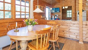 L’intérieur d’un chalet en bois comprend une table de salle à manger ronde, des chaises, un vase avec des fleurs et un coin cuisine avec des placards et des appareils électroménagers.