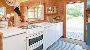 A cabin-style kitchen with wooden walls, a large island with a stove and oven, hanging lights, and a view of the outdoors. - Charming Coastal Retreat-by Traum (Jerup)