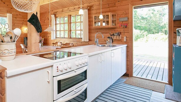 Une cuisine de style rustique, avec des murs en bois, un grand îlot central doté d’une cuisinière et d’un four, des luminaires suspendus et une vue sur l’extérieur.