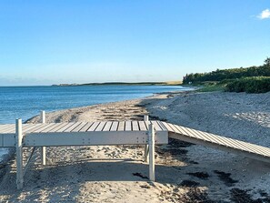 A wooden boardwalk leading to a sandy beach with a clear view of the ocean.
