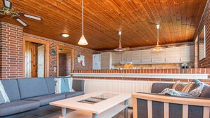 Un intérieur chaleureux avec un mur en briques, un plafond en bois, un canapé, une table et un coin cuisine doté de placards et d’un plan de travail.