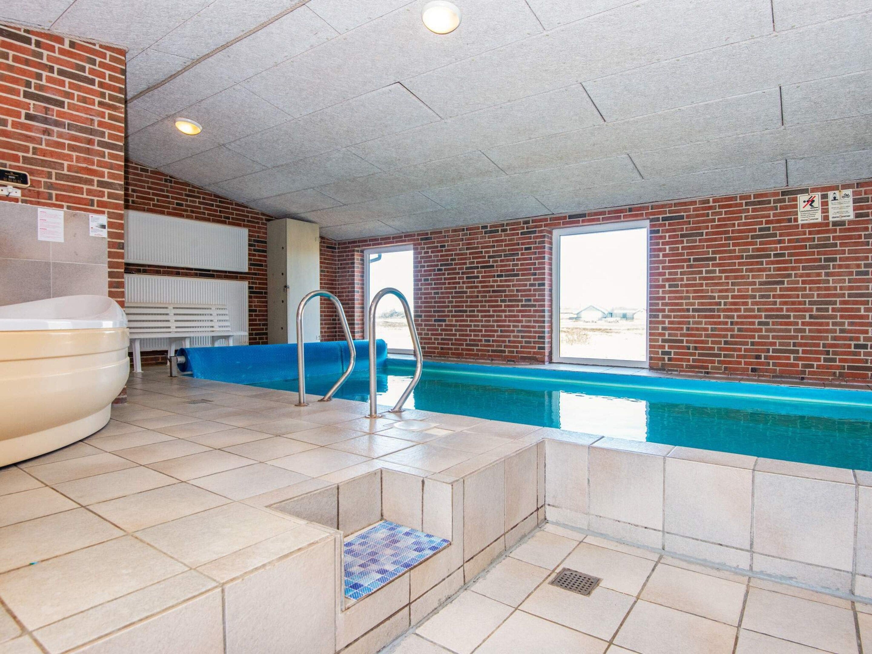 Zona de piscina con pared de ladrillo, jacuzzi y ventana con vistas.