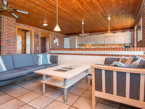 A cozy interior with a wooden ceiling, a brick wall, a sofa, a table, and a kitchen area.