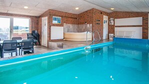 Une piscine intérieure avec un mur en briques, un jacuzzi et un espace détente avec des fauteuils.