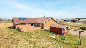 Une maison de plain-pied en briques, avec un toit en pente, un petit abri de jardin rouge attenant et une cour gazonnée.