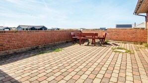 Un espace extérieur aménagé en patio, avec un sol en briques, un mur en briques et un banc rouge.
