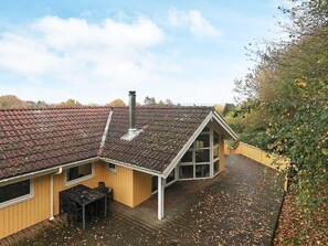 Una casa con techo inclinado, chimenea, terraza y vistas a árboles.