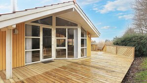 A wooden deck with a covered patio area, large sliding glass doors, and a chimney. - 10 Person Holiday Home in Rudkobing (Rudkobing)