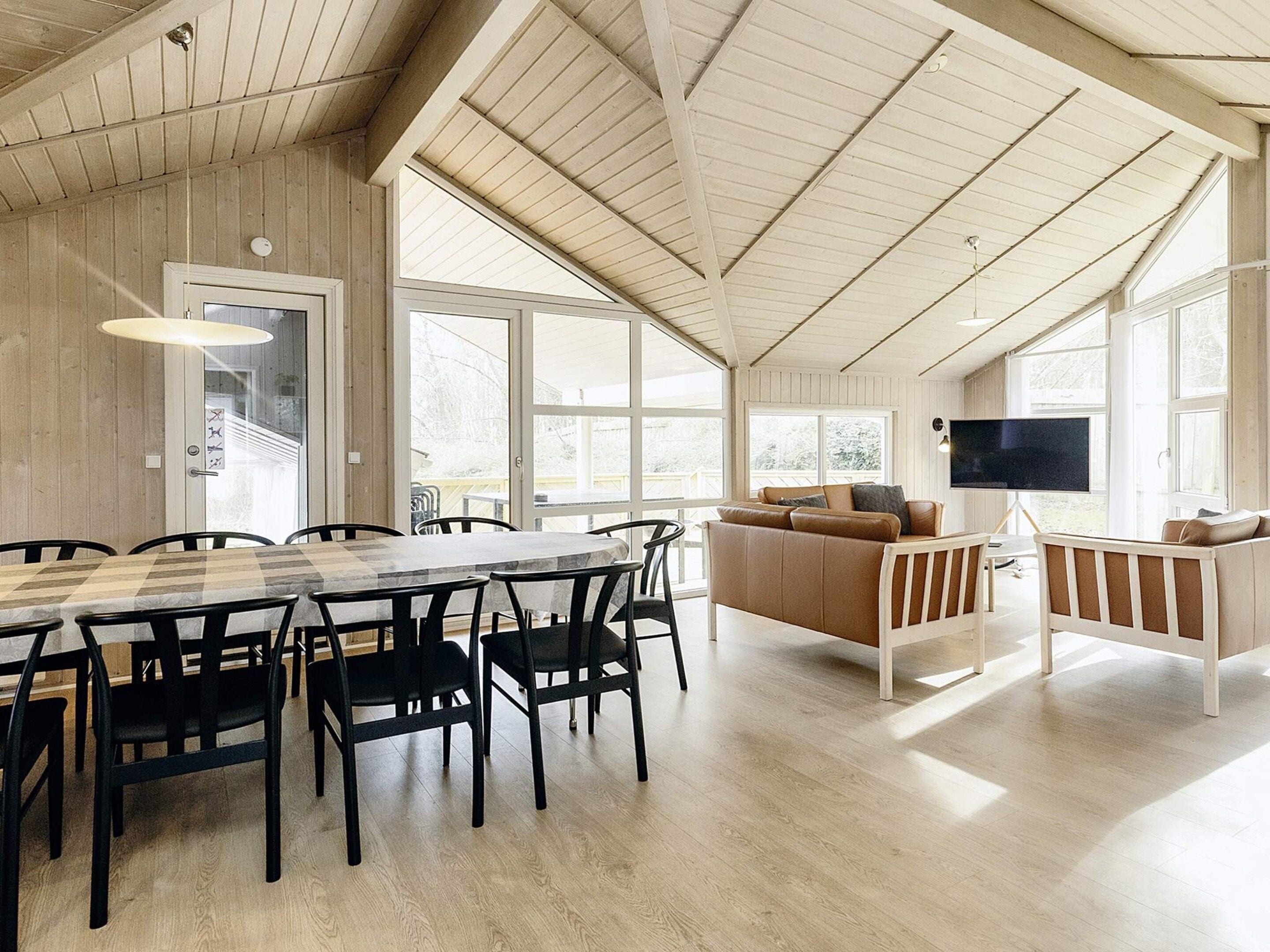 A spacious room with a high ceiling, a dining area with a wooden table and chairs, a sofa, and a television.