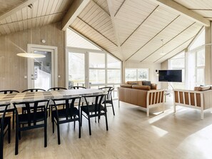 A spacious room with a high ceiling, a dining area with a wooden table and chairs, a sofa, and a television. - 10 Person Holiday Home in Rudkobing (Rudkobing)